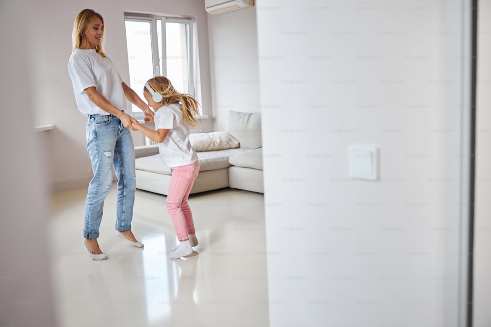 Portrait of young happy elegant mother dancing with little cute daughter in big white living room in their apartment at the vacation
