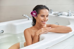 Bella signora con fiore viola tra i capelli che distoglie lo sguardo e sorride mentre fa il bagno
