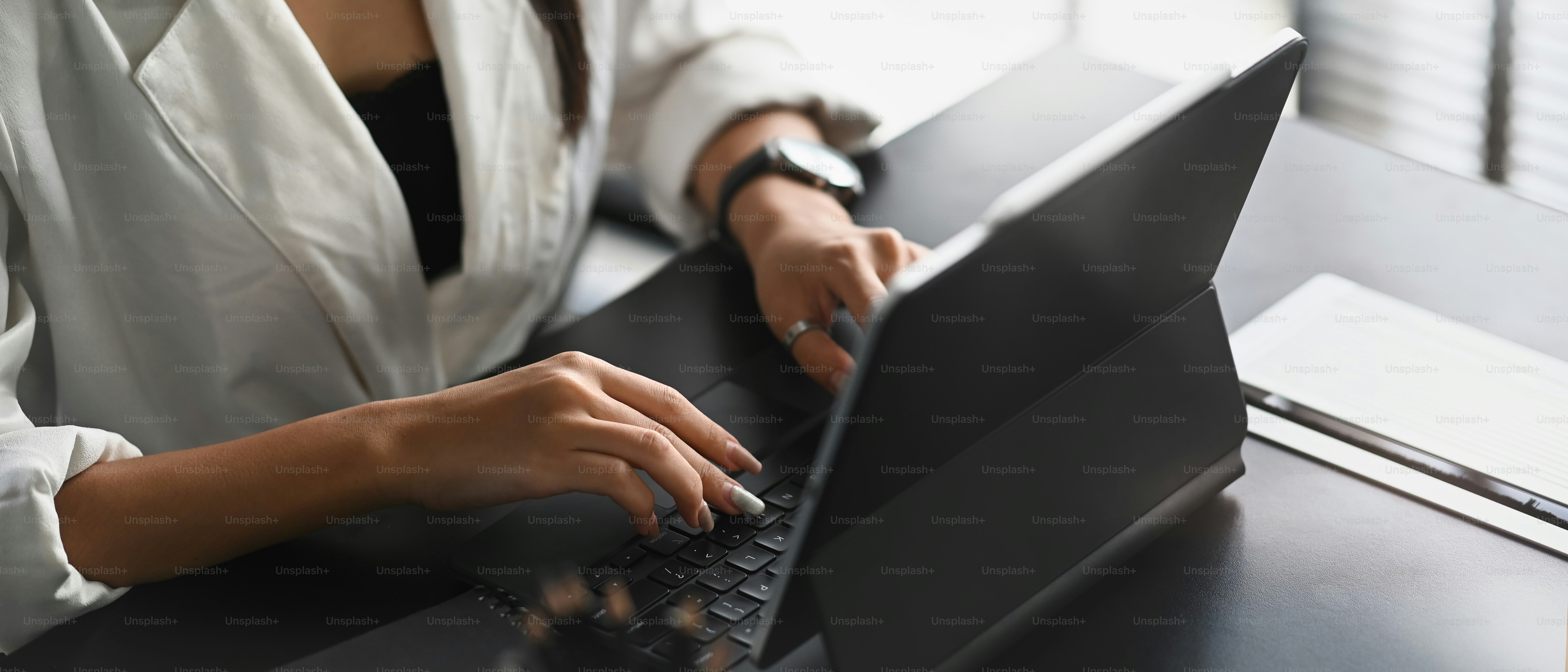 Cropped shot of businesswoman working with computer tablet on black wooden table in modern office.
