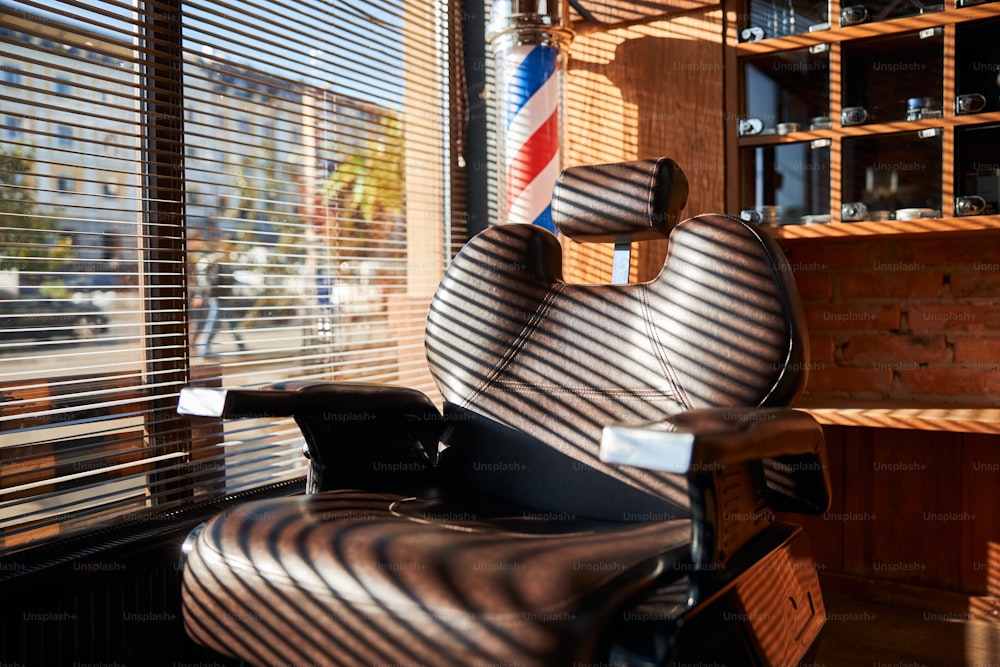 Close up de cadeira de barbeiro de couro marrom resistente e reclinável pela janela com persianas