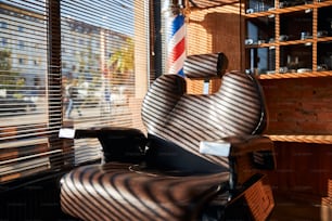 블라인드가 있는 창가에 기대어 있는 튼튼하고 기대어 있는 갈색 가죽 이발소 의자를 닫습니다.