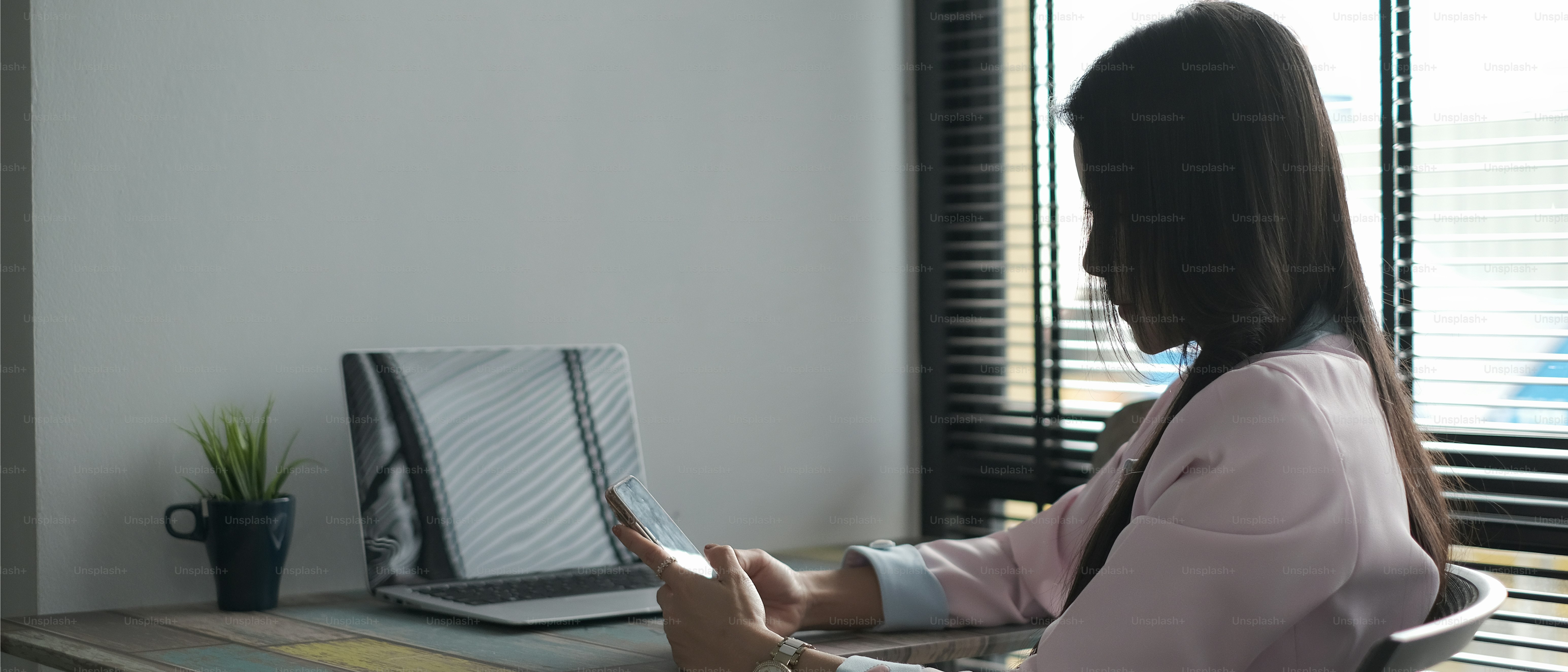 A young female using smartphone while sitting at office desk in office.