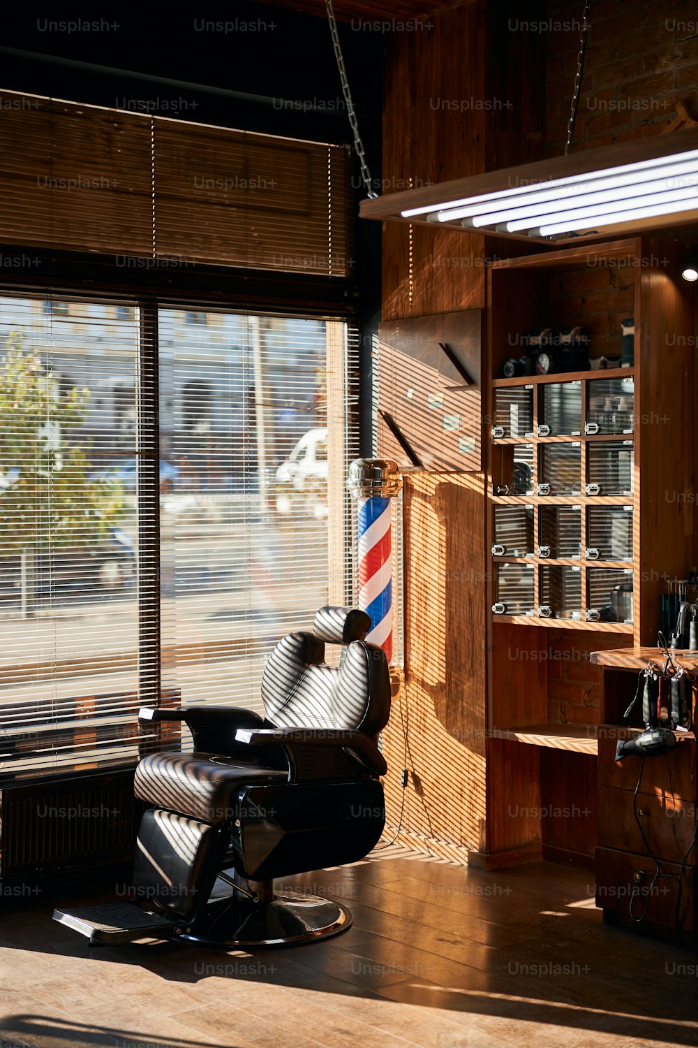 Sillón de barbero de cuero reclinable con reposacabezas ajustable ubicado junto a la ventana con persianas en salón de peluquería
