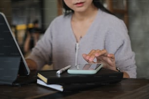 Foto recortada de una mujer joven que trabaja con una tableta de maqueta mientras busca información en un teléfono inteligente en la oficina.