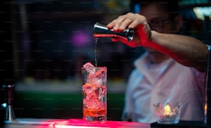 Männlicher Barkeeper gießt alkoholisches Schnapsgetränk aus Jigger in langes Cocktailglas