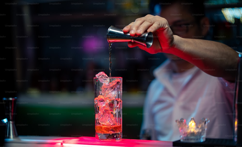 Barman masculin versant une boisson alcoolisée à partir d’un jigger dans un long verre à cocktail
