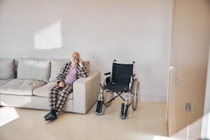 Personne âgée en pantoufles et pyjama assise sur le canapé pendant la conversation téléphonique