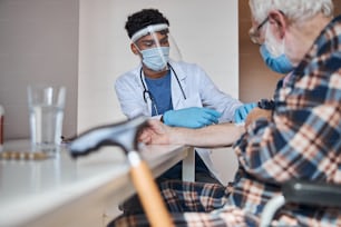 Jeune médecin sérieux portant un masque facial administrant une injection à un retraité masculin