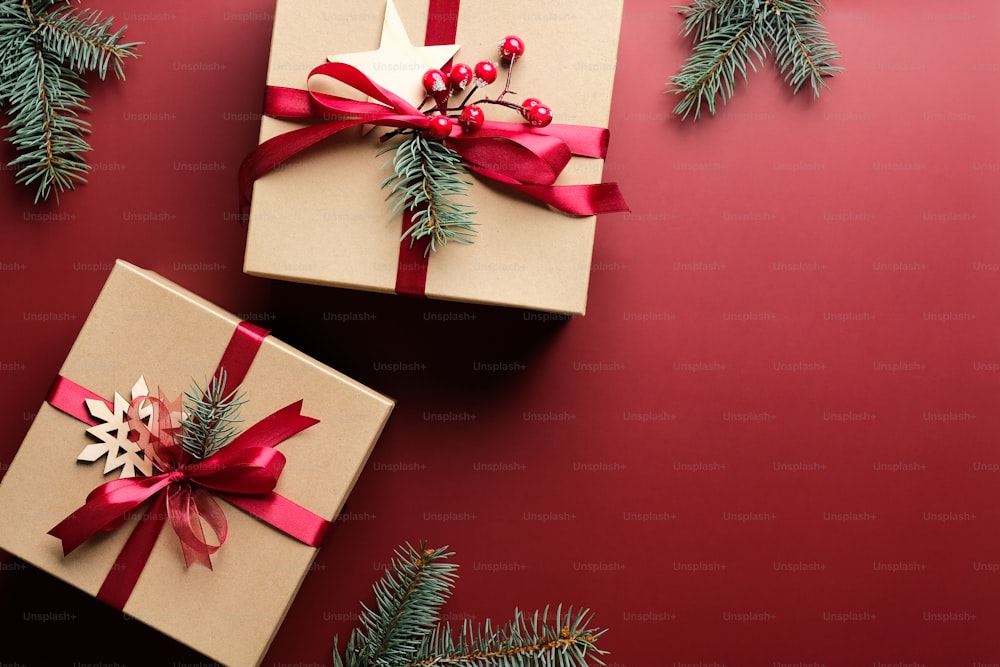 Scatole regalo natalizie con fiocco in nastro rosso e decorazioni su fondo rosso marsala. Posa piatta, vista dall'alto. Regali di Natale.