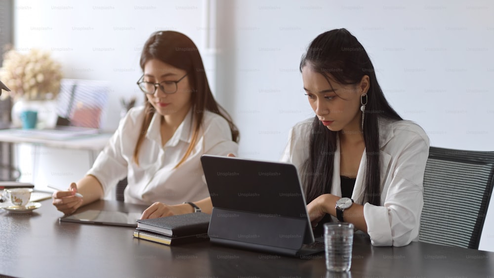 Two young female businesspeople working together in meeting room with office supplies