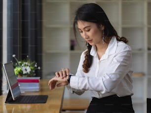 Young female office worker checking on time with her watch in office room