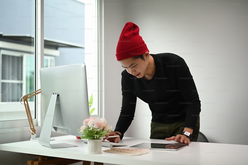 A Graphic designer man in red wool hat is working on his new project in creative office.