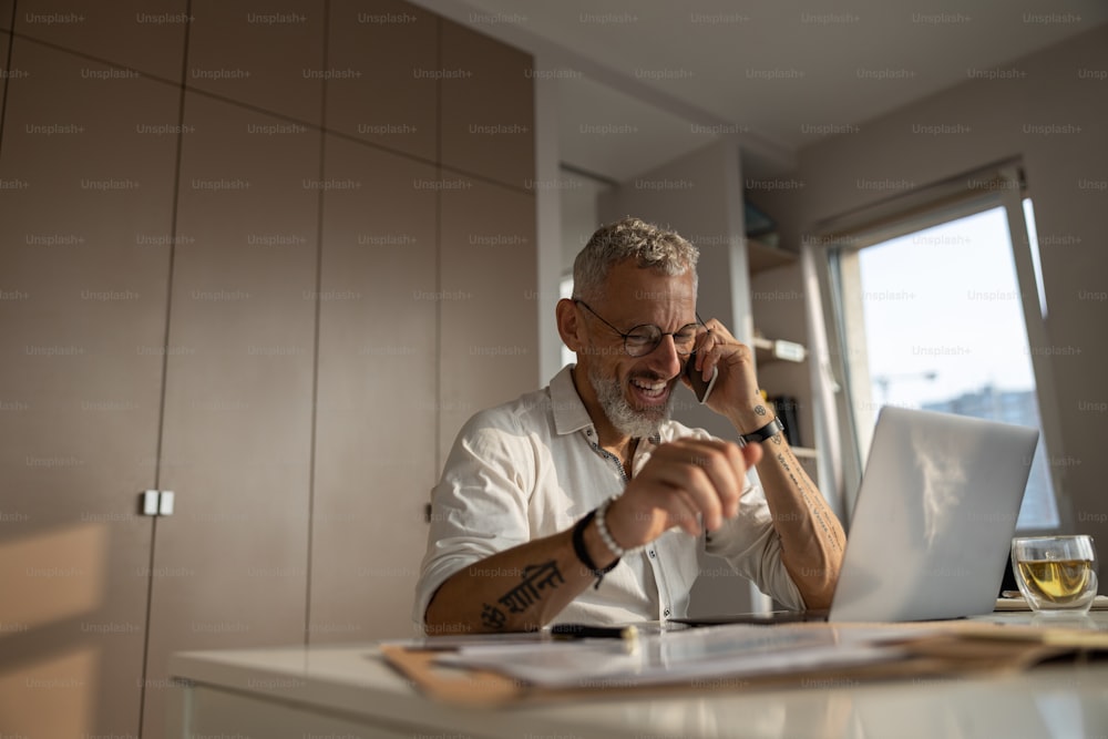 Homme d’affaires énergique gardant un téléphone portable près de son oreille alors qu’il est assis à son bureau dans un bureau