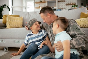 Soldado feliz sentado en el suelo con su familia. Soldado disfrutando en casa con niños.
