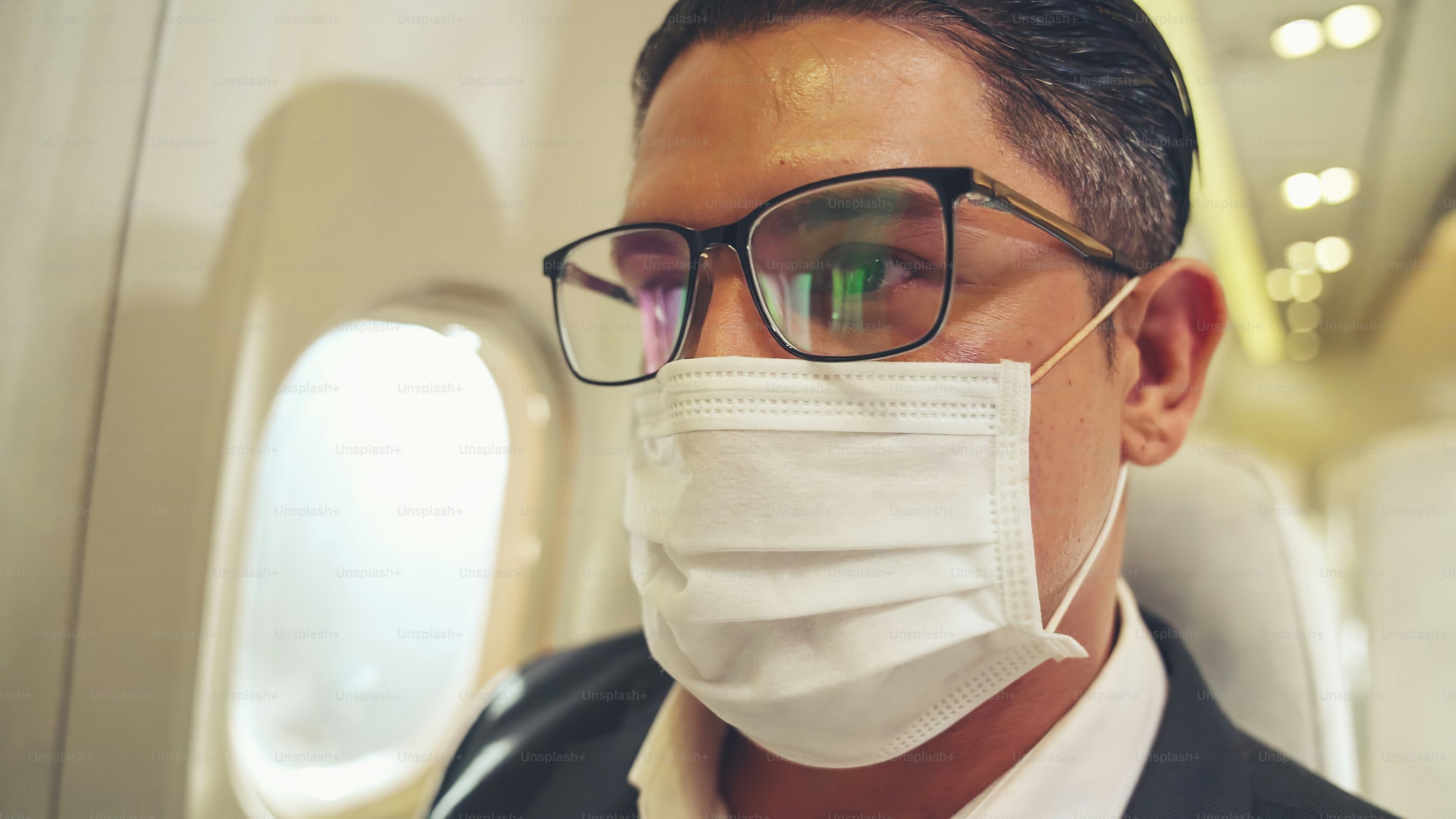 Traveler wearing face mask while traveling on commercial airplane . Concept of coronavirus disease or COVID 19 pandemic outbreak effects on tourism and airline business .