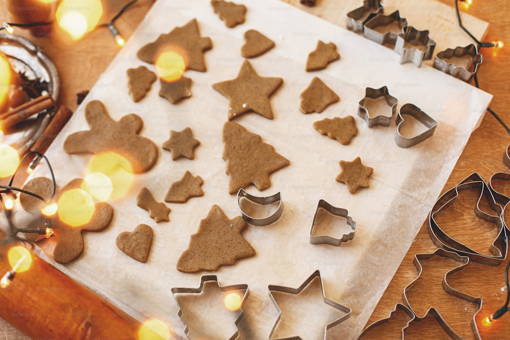 Biscuits au pain d’épices crus dans des formes festives de Noël et des emporte-pièces en métal, des décorations et des lumières sur une table rustique. Cuisson de biscuits au pain d’épices, vacances de Noël avènement.
