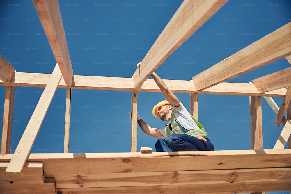 Kind builder working high on the roof of future house and wearing special uniform