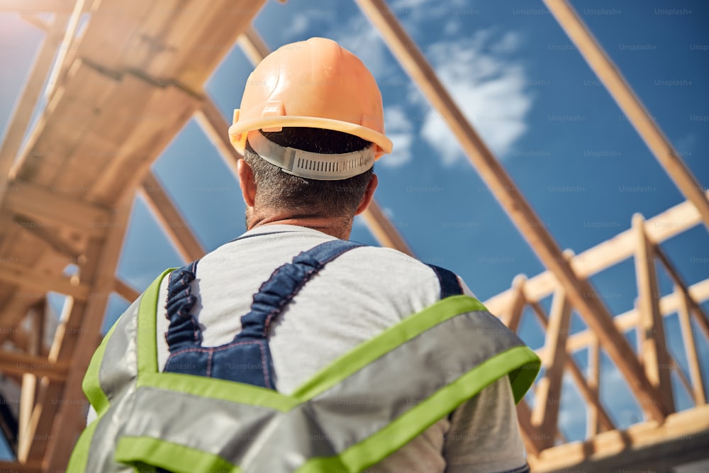 Attentive male person wearing helmet while being at work, preparing beams for making the roof