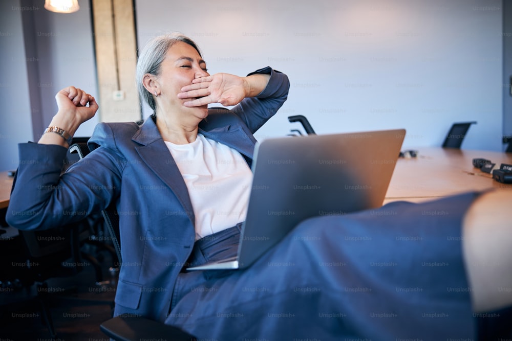 Elegante Geschäftsfrau, die schläfrig und müde ist, während sie im Büro an einem Notebook arbeitet