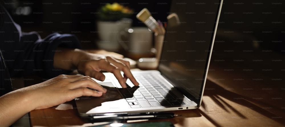 Seitenansicht der weiblichen Hand, die auf dem Laptop auf einem Holztisch mit Zubehör und Dekorationen tippt