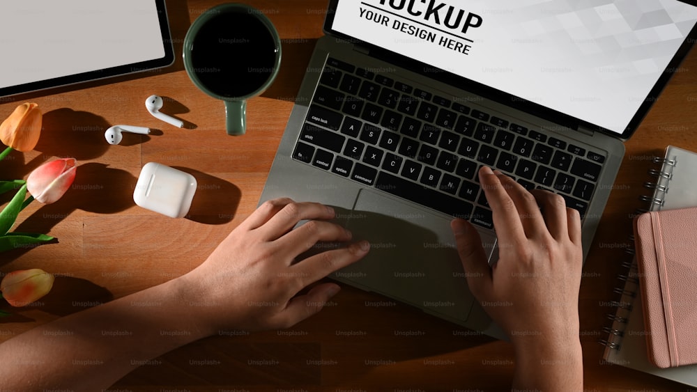 Top view of male hands typing on laptop on wooden table with supplies and flower, include clipping path