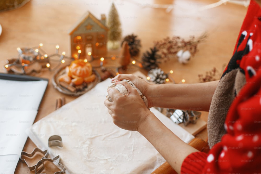 Mains pétrissant de la pâte à pain d’épice crue sur fond de coupeurs en métal, d’épices, d’oranges, de décorations festives sur une table rustique. Personne faisant des biscuits en pain d’épice, tradition de vacances de Noël