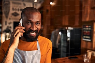 Bel ouvrier masculin en tablier ayant une conversation téléphonique et souriant