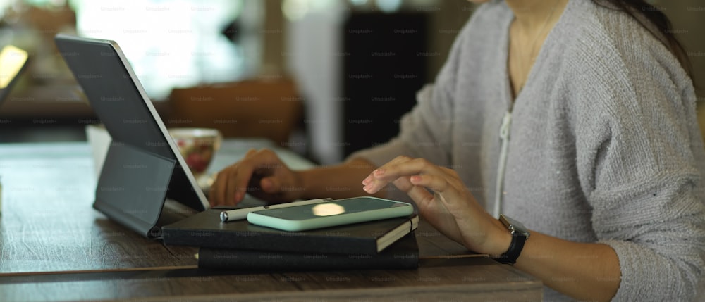 Side view of female freelancer hand working with digital tablet, notebook and smartphone on wooden table