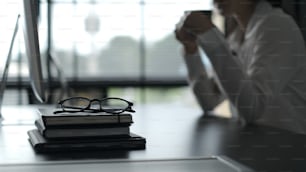 A glasses placing on top of the pile of books in office.