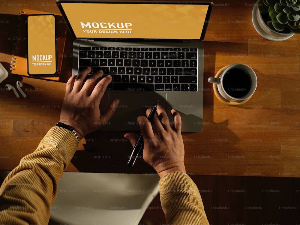 스마트폰과 커피 컵이 있는 노트북에서 남성 손으로 타이핑하는 오버헤드 샷, 나무 테이블에 있는 커피 컵, 클리핑 경로