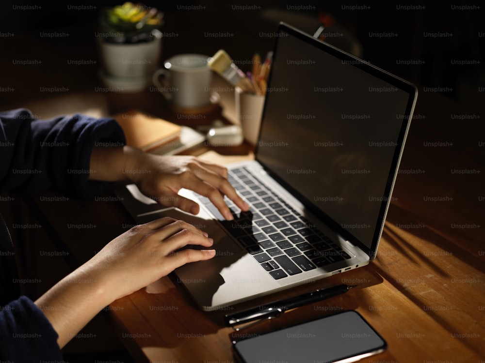 Vista laterale della digitazione a mano femminile sul computer portatile sul tavolo di legno con smartphone e forniture