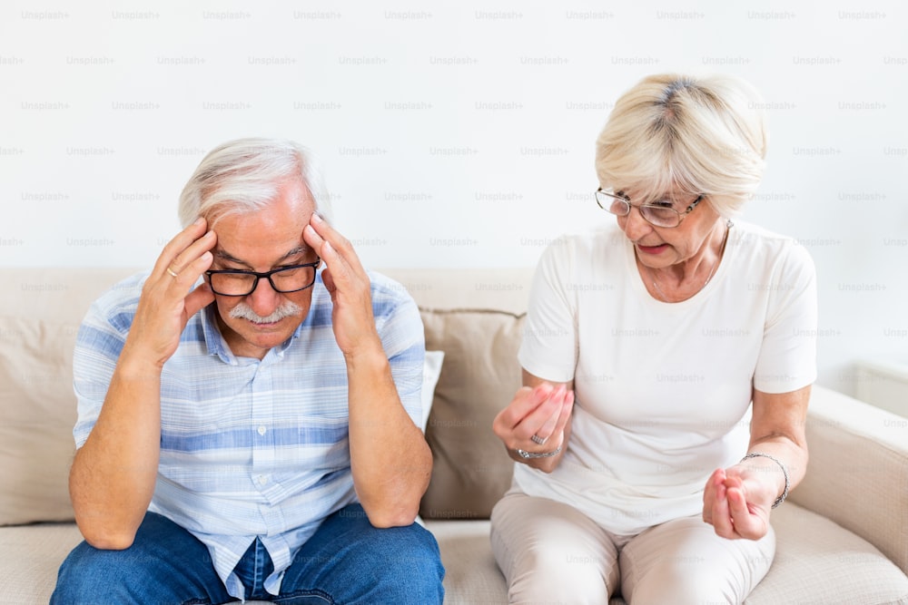 Älteres Ehepaar streitet. Älterer Mann mit Kopfschmerzen, hält seinen Kopf zwischen den Händen. Reife Frau frustriert von ihrem Ehemann. Heiratsprobleme