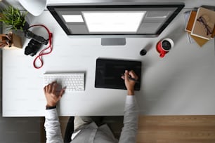 Over head shot of professional photographer using a graphic tablet and stylus pen editing his pictures at his workspace.