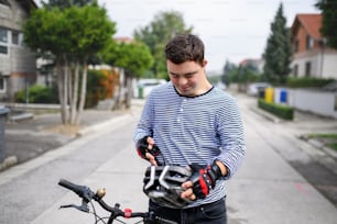 Portrait of down syndrome adult man with bicycle and helmet standing outdoors on street.