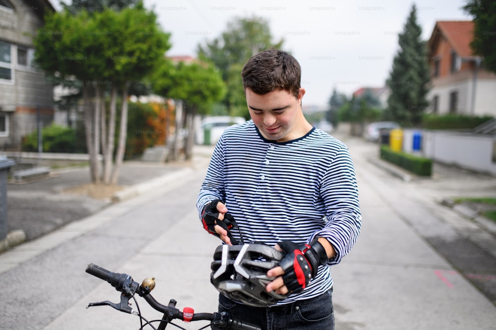 Porträt des erwachsenen Mannes mit Down-Syndrom mit Fahrrad und Helm, der draußen auf der Straße steht.