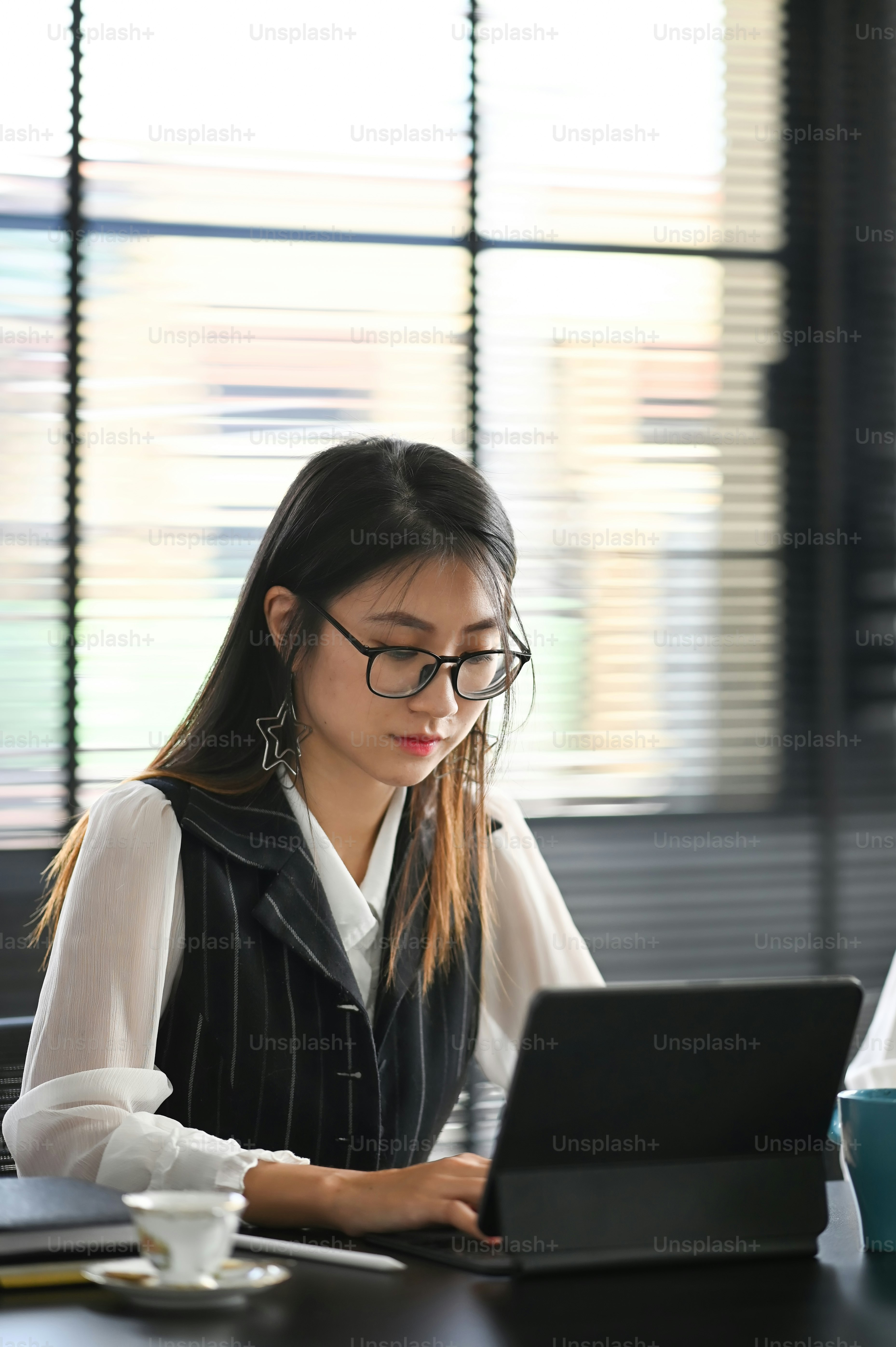 Portrait of young business woman in glasses working on computer tablet while sitting at workplace.