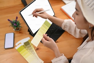 A young graphic designer working on digital tablet and using colour swatch samples in office.