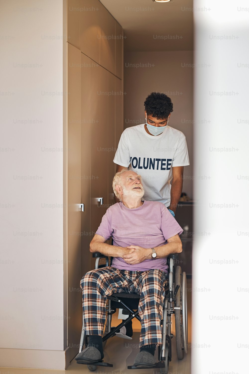 Vorderansicht eines älteren kaukasischen Mannes im Rollstuhl, der zu seiner Pflegerin aufblickt