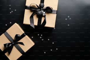 Cardboard gift boxes decorated black ribbon bows and confetti on black background. Christmas present, New Year gift box concept.