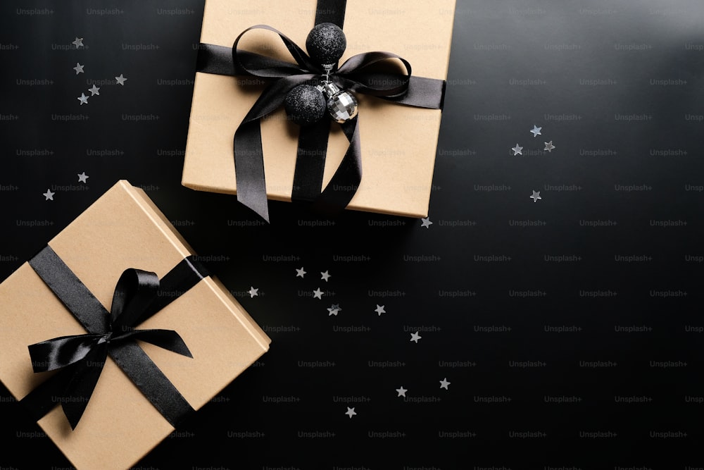 Cardboard gift boxes decorated black ribbon bows and confetti on black background. Christmas present, New Year gift box concept.