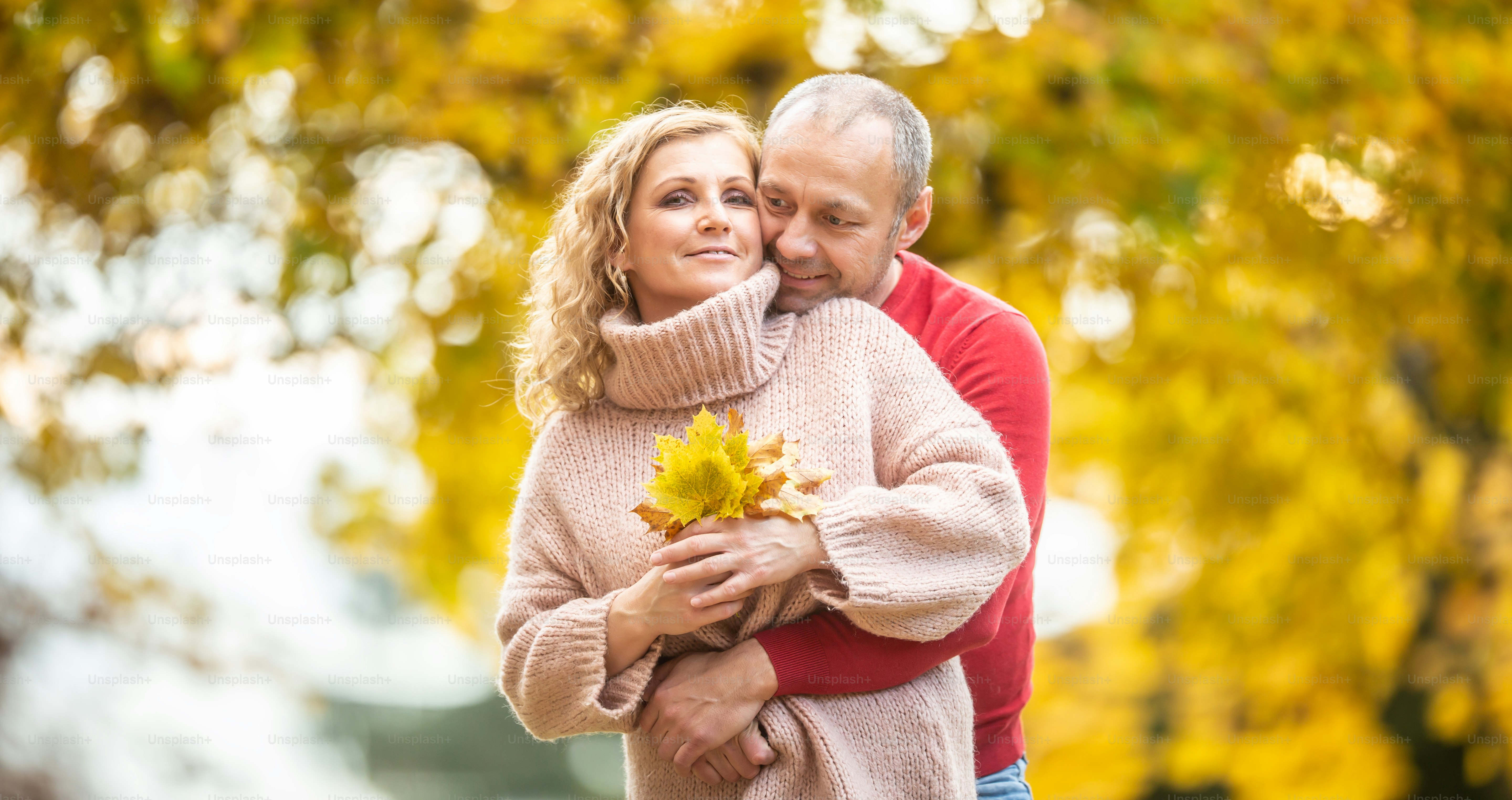La pareja comparte su amor abrazándose, sosteniendo hojas caídas de otoño  rodeadas de árboles amarillos. foto – Imagen de Al aire libre en Unsplash, image size:3000x1588