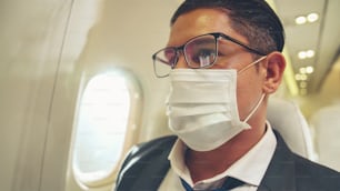 Viaggiatore che indossa una maschera facciale durante il viaggio su un aereo commerciale. Concetto di malattia da coronavirus o effetti dell'epidemia di pandemia COVID 19 sul turismo e sul business delle compagnie aeree.