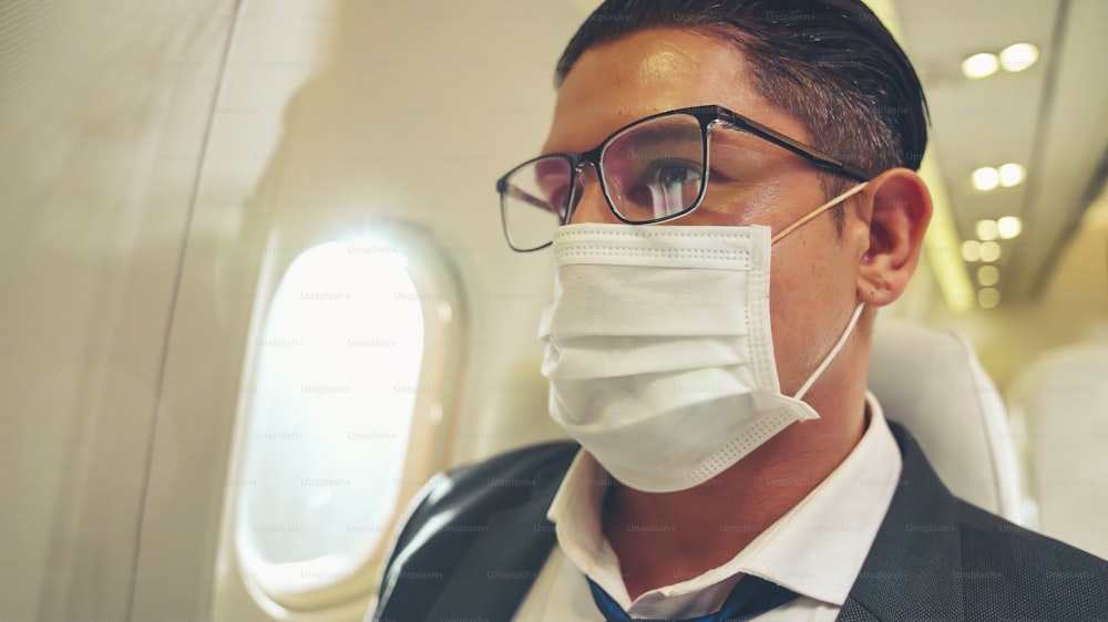 Traveler wearing face mask while traveling on commercial airplane . Concept of coronavirus disease or COVID 19 pandemic outbreak effects on tourism and airline business .