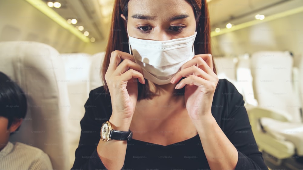 Traveler wearing face mask while traveling on commercial airplane . Concept of coronavirus disease or COVID 19 pandemic outbreak effects on tourism and airline business .