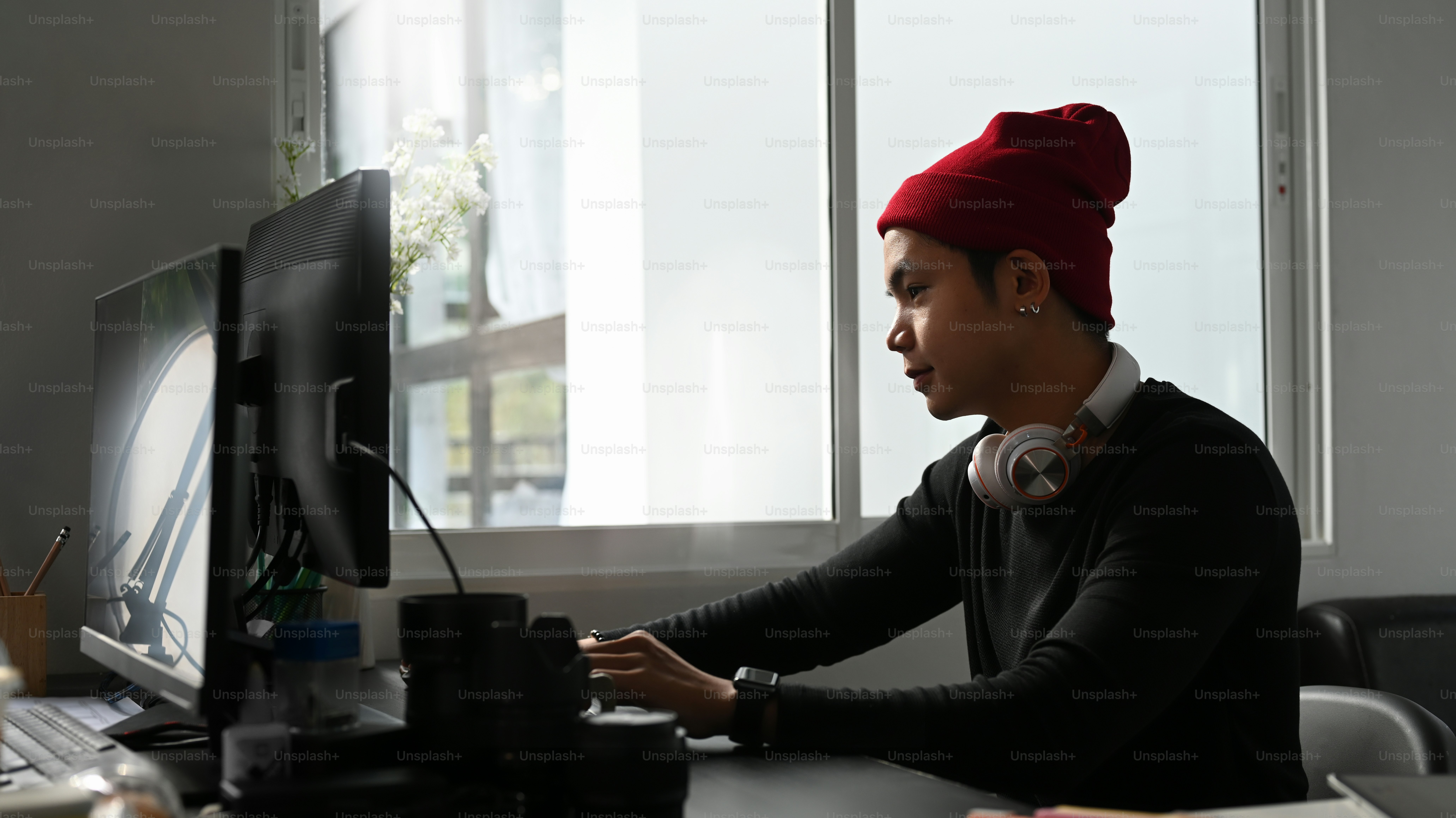 Vue latérale d’un jeune photographe en bonnet de laine rouge travaillant sur un nouveau projet sur ordinateur dans son studio.