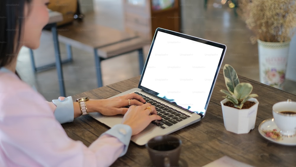 Una mujer de negocios escribiendo en una computadora portátil con la pantalla vacía en su lugar de trabajo.