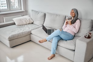 Full length portrait of happy cheerful woman in casual clothes sitting on the sofa in room indoors