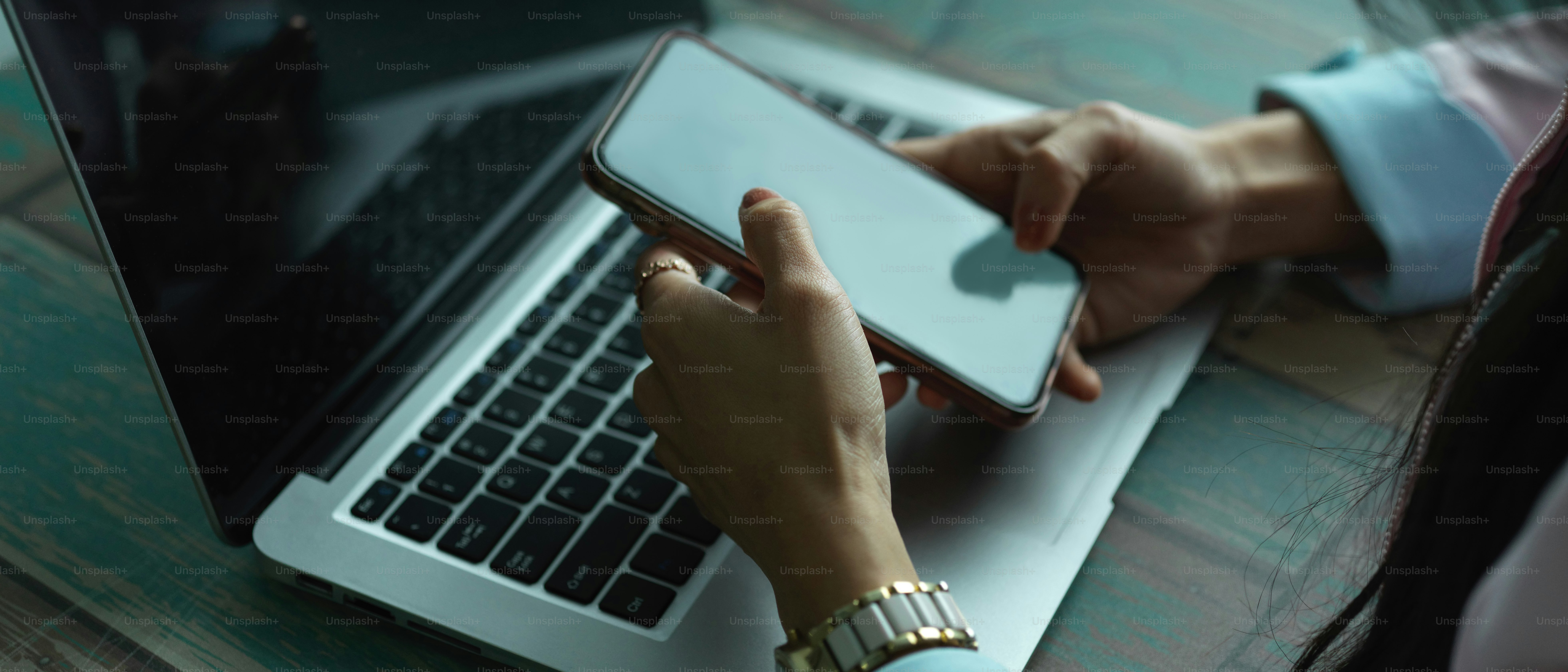 Cropped shot of female hands using smartphone while working with laptop in office room