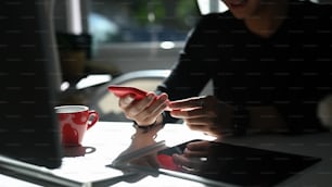 若い男性が仕事場に座り、携帯電話でソーシャルメディアを共有しながらメッセージを打ち込んでいる様子を撮影した写真。