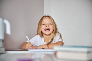 Close up of funny charming small miss in white shirt spending time at home while learning exercises on mathematics